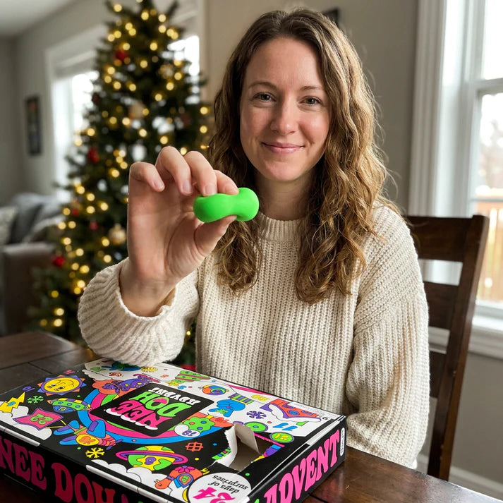 Product lifestyle image showing a mini green toy held above the NeeDoh advent calendar
